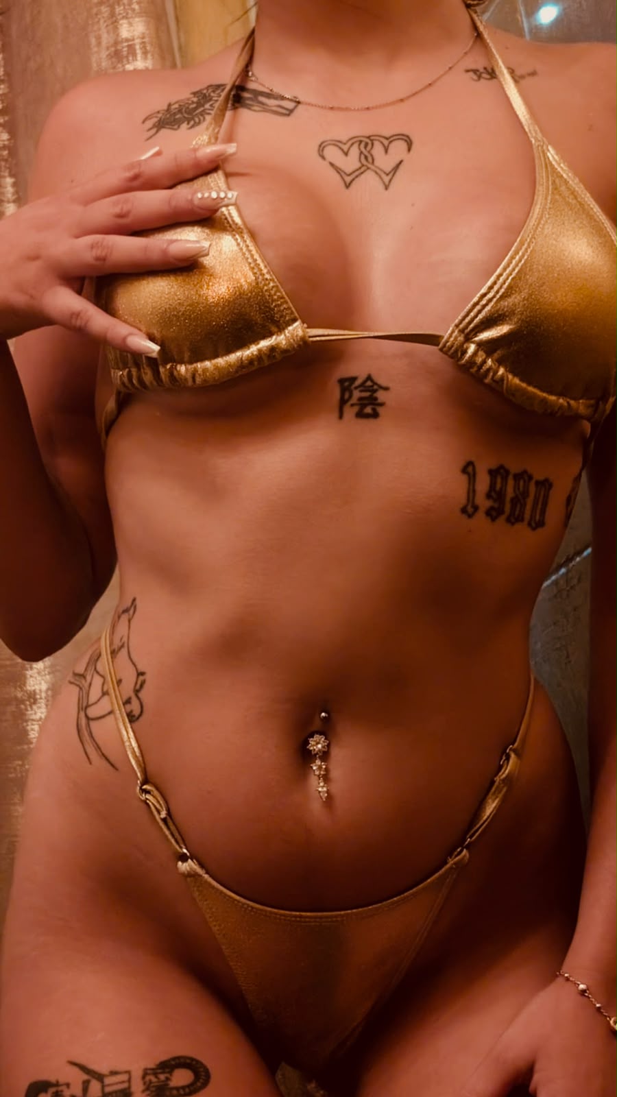 Close-up of a performer in a gold bikini showing tattoos and a navel piercing